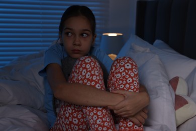 Photo of Fearful girl sitting on bed at night