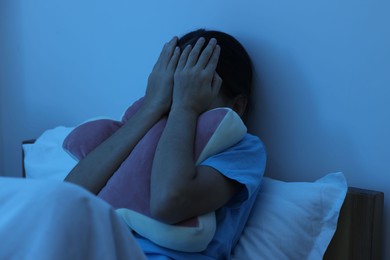 Photo of Afraid girl covering face with hands in bed at night