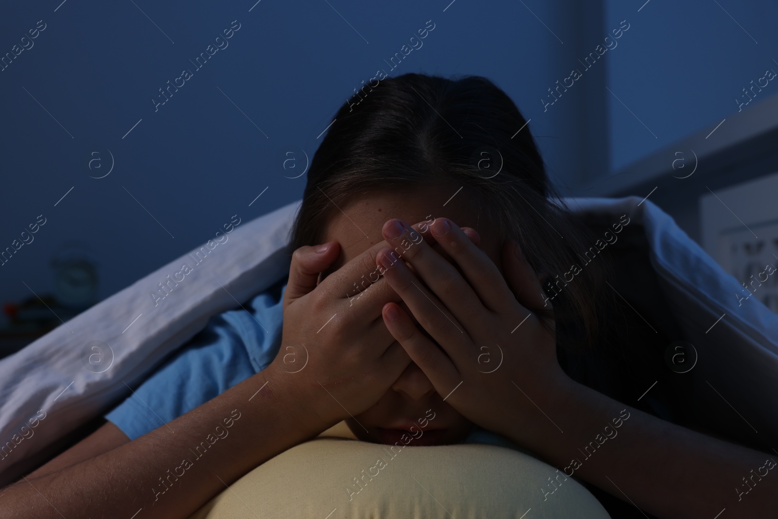 Photo of Afraid girl with pillow under duvet on bed at night