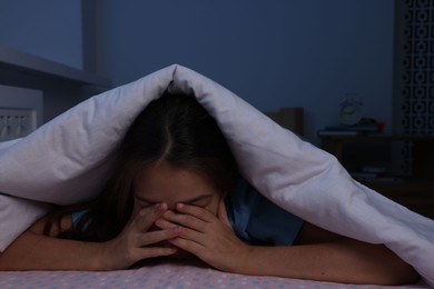 Photo of Afraid girl hiding under duvet on bed at night