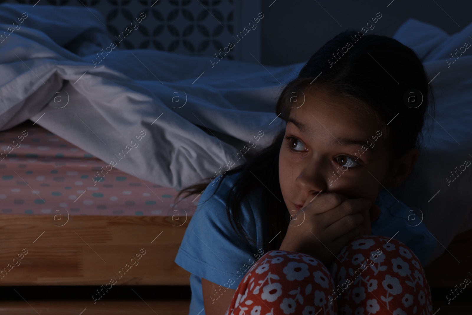 Photo of Afraid girl near bed in her room at night. Space for text