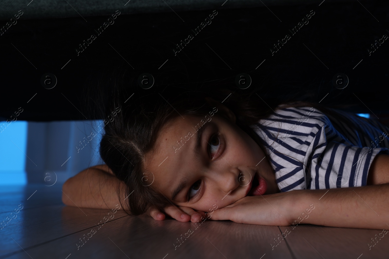 Photo of Fearful girl hiding under bed at night