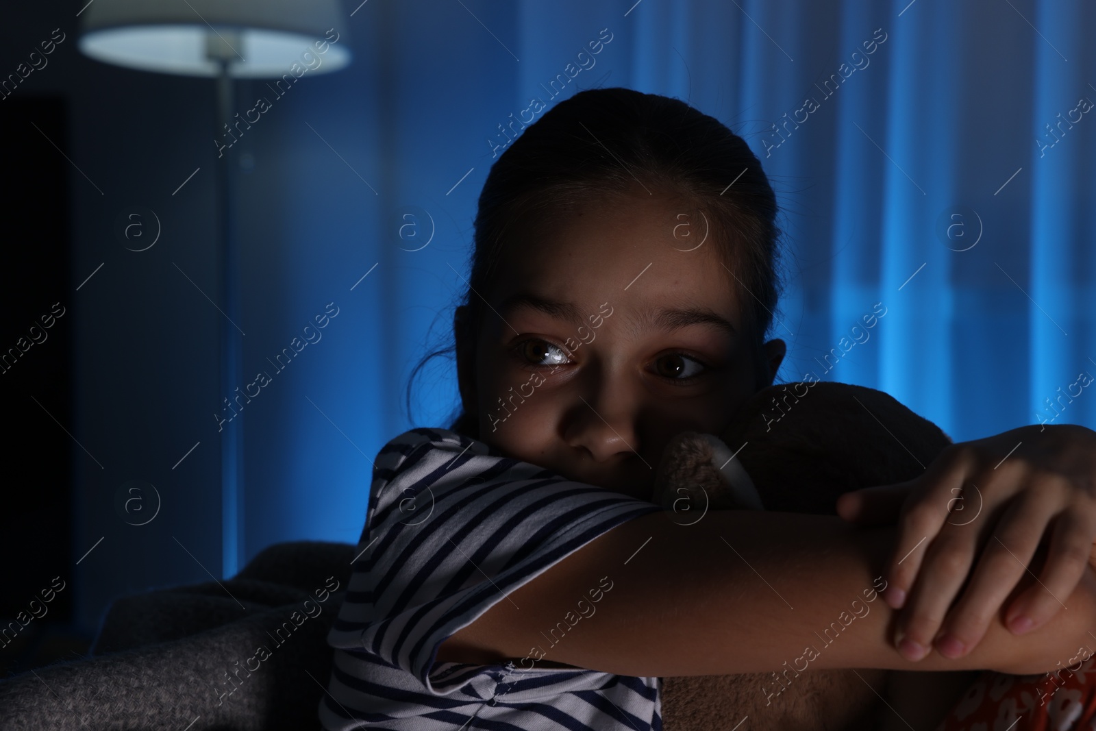 Photo of Afraid girl with teddy bear on sofa at home