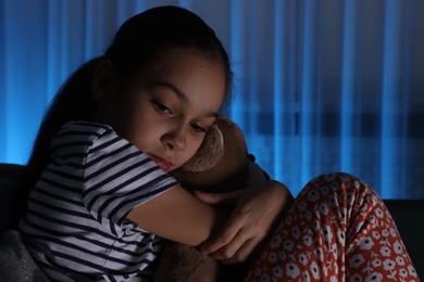 Photo of Afraid girl with teddy bear on sofa at home