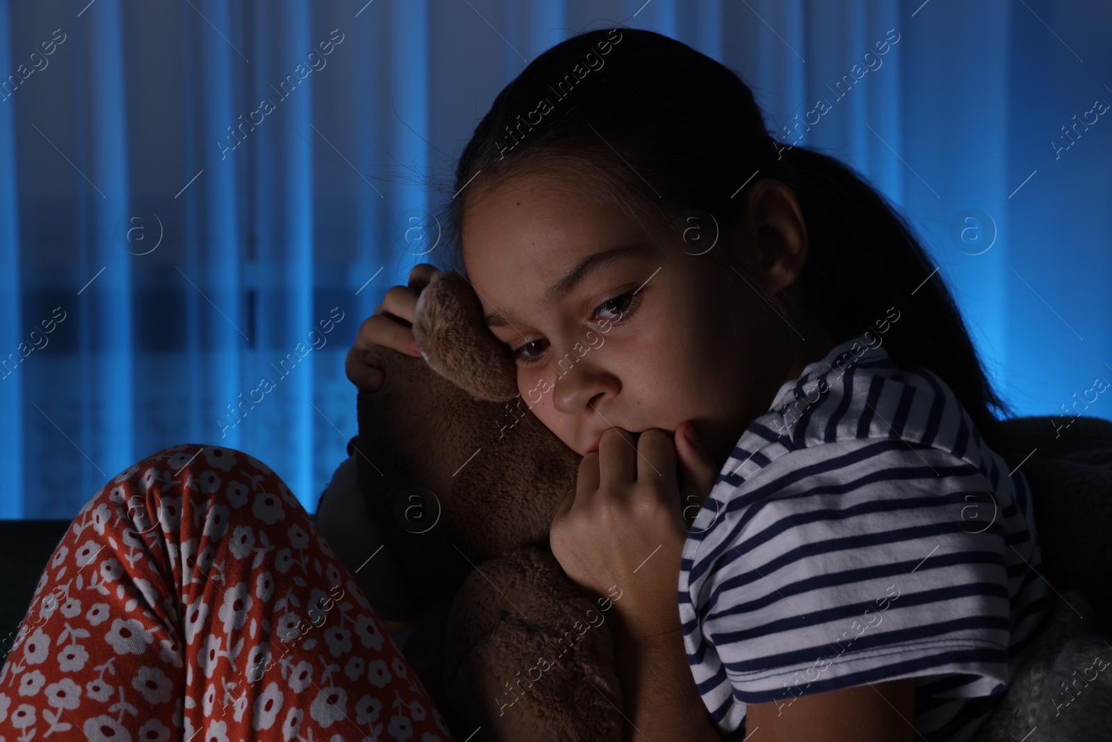 Photo of Afraid girl with teddy bear on sofa at home