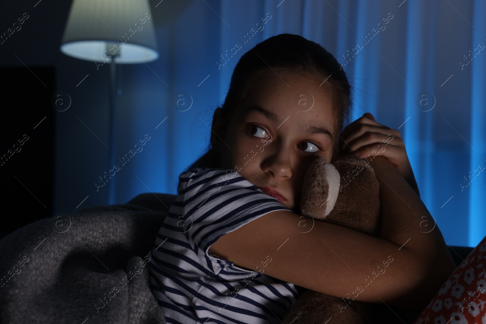 Photo of Afraid girl with teddy bear on sofa at home