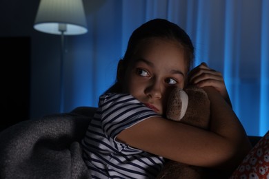 Photo of Afraid girl with teddy bear on sofa at home