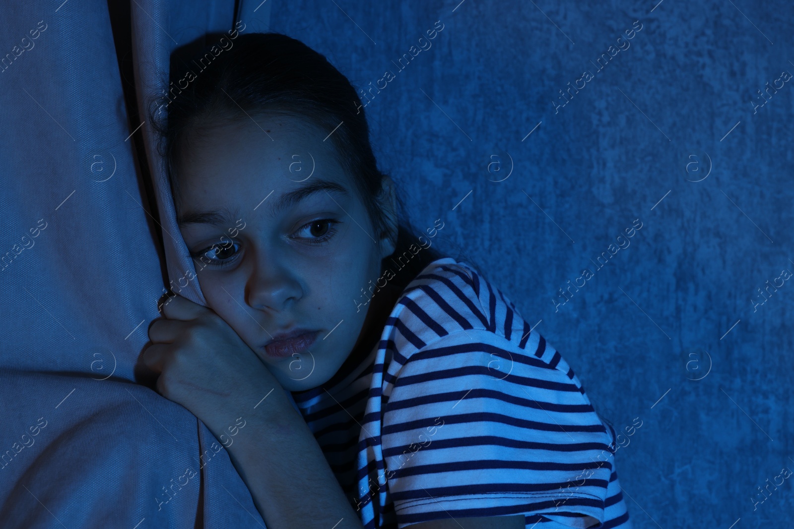 Photo of Scared girl hiding behind curtain at night. Space for text