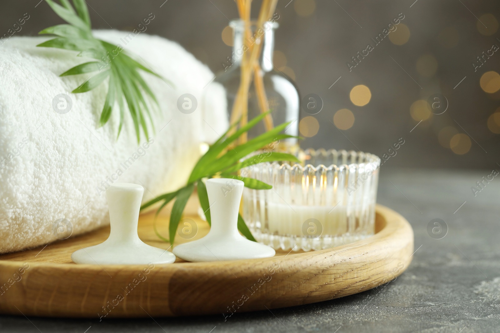 Photo of Spa stones, burning candle, towel and green leaves on grey table, closeup