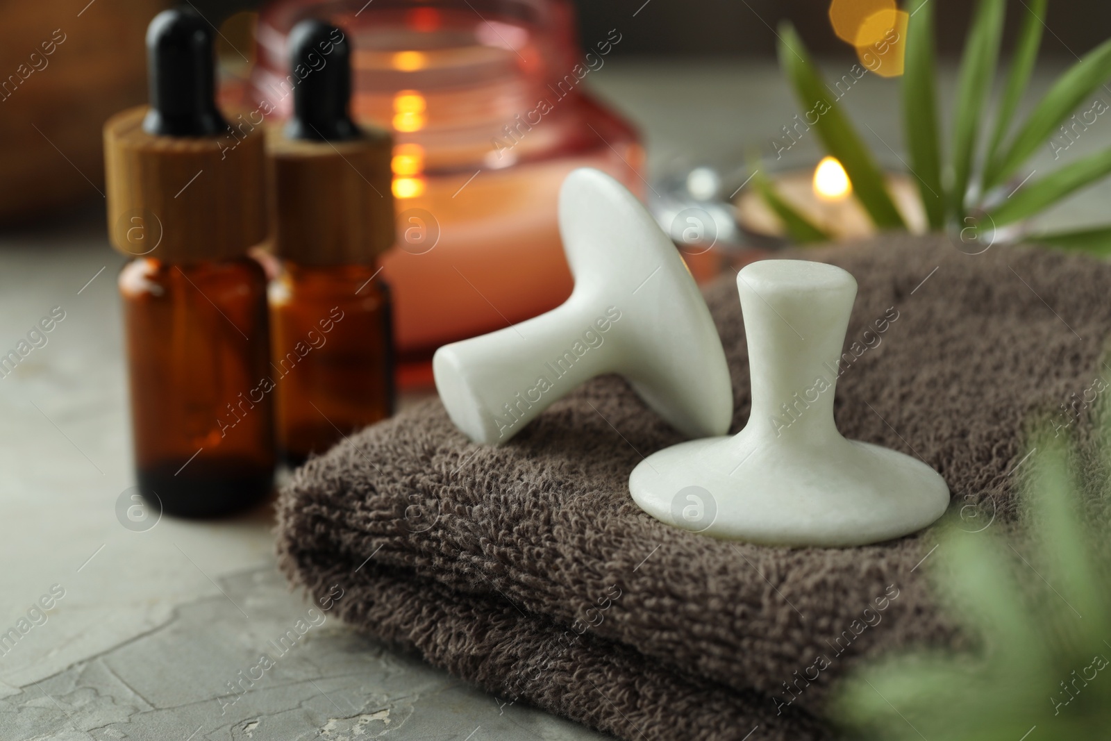 Photo of Spa stones, towel, cosmetic products, candle and green leaves on grey table, closeup