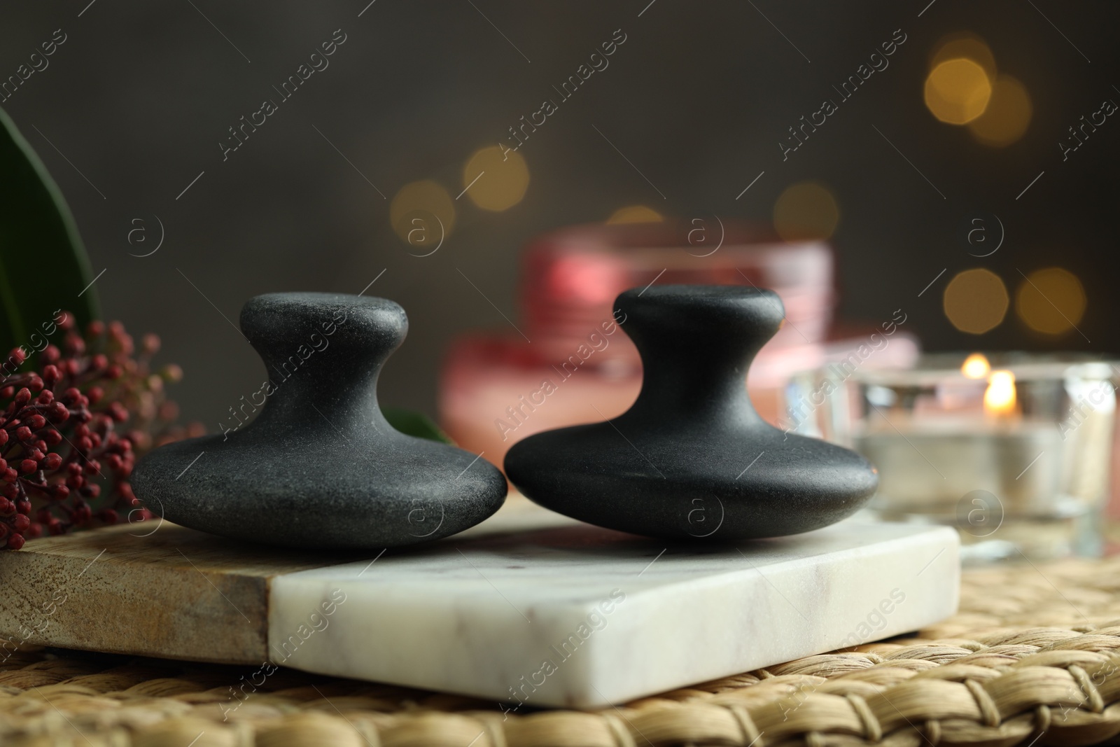 Photo of Spa stones, floral decor and candle on wicker mat, closeup