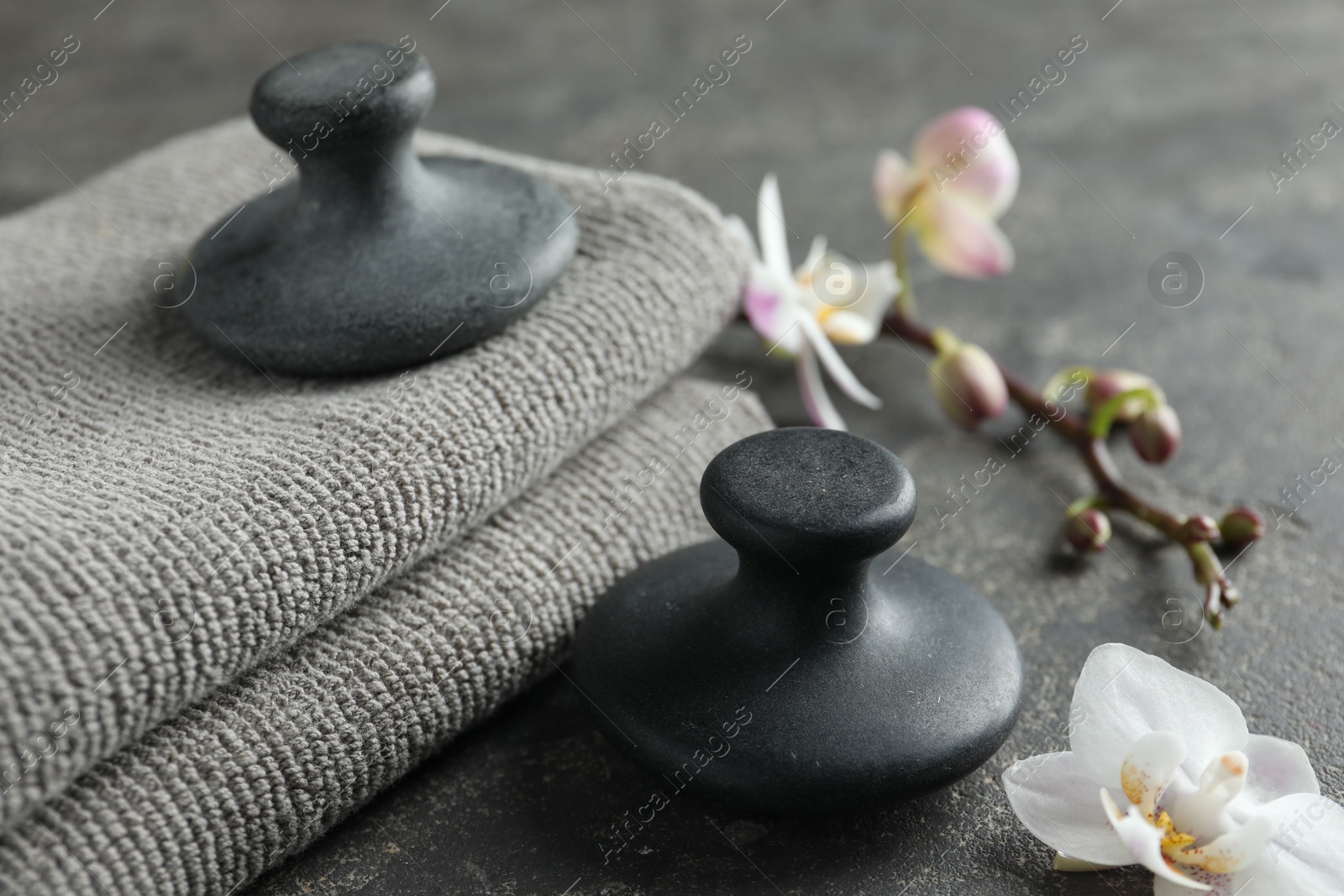 Photo of Spa stones, towels and orchid flowers on grey table, closeup