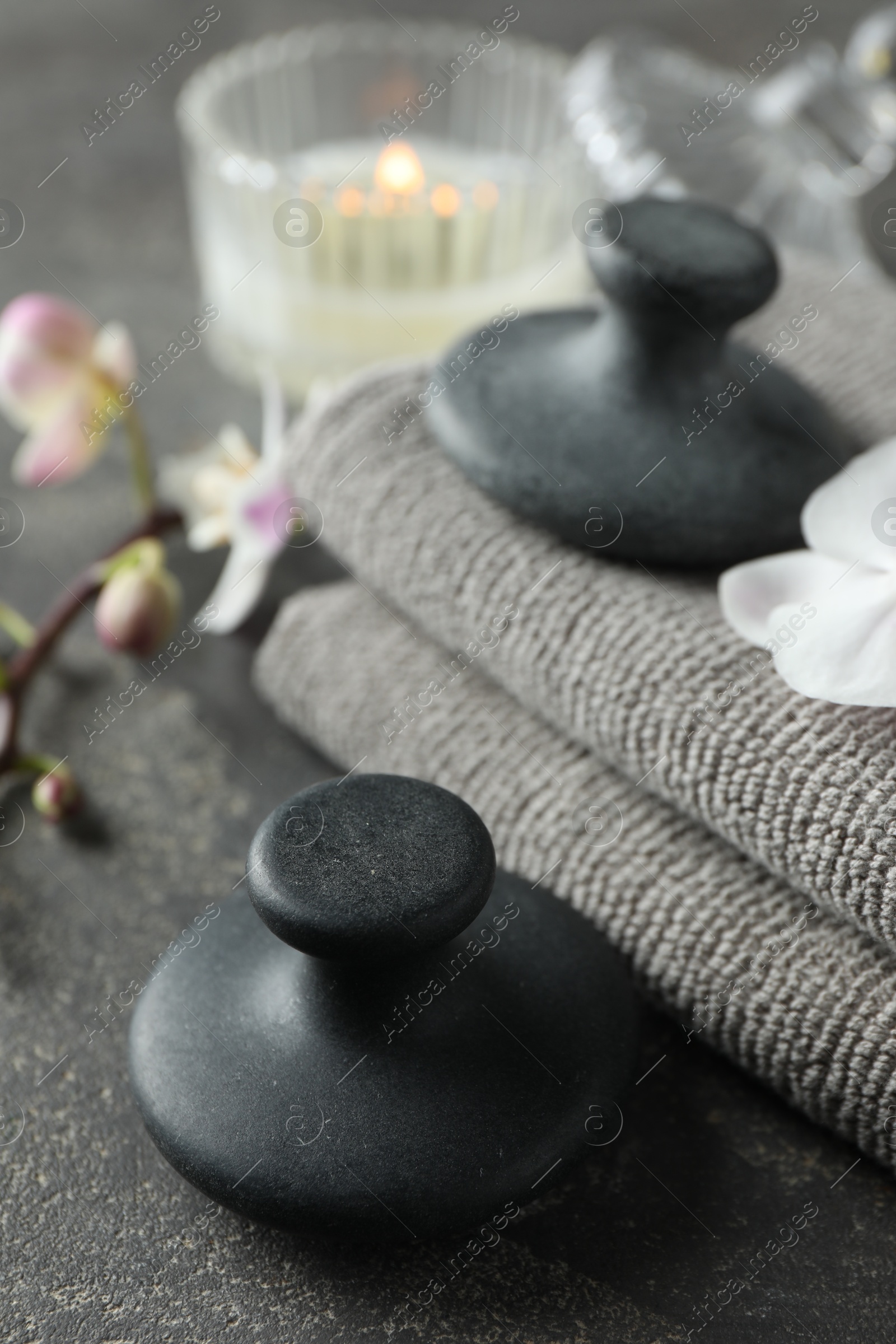 Photo of Spa stones, towels, orchid branch and candle on grey table, closeup