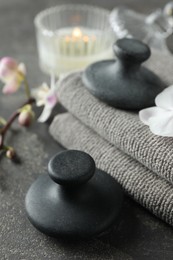 Photo of Spa stones, towels, orchid branch and candle on grey table, closeup