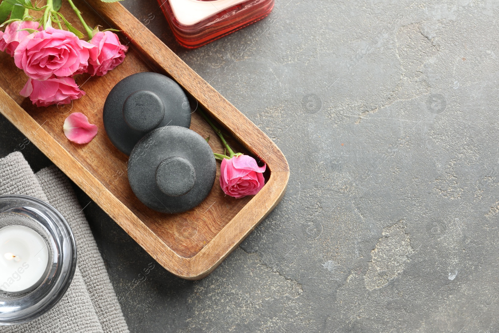 Photo of Spa stones, rose flowers and candles on grey table, flat lay. Space for text