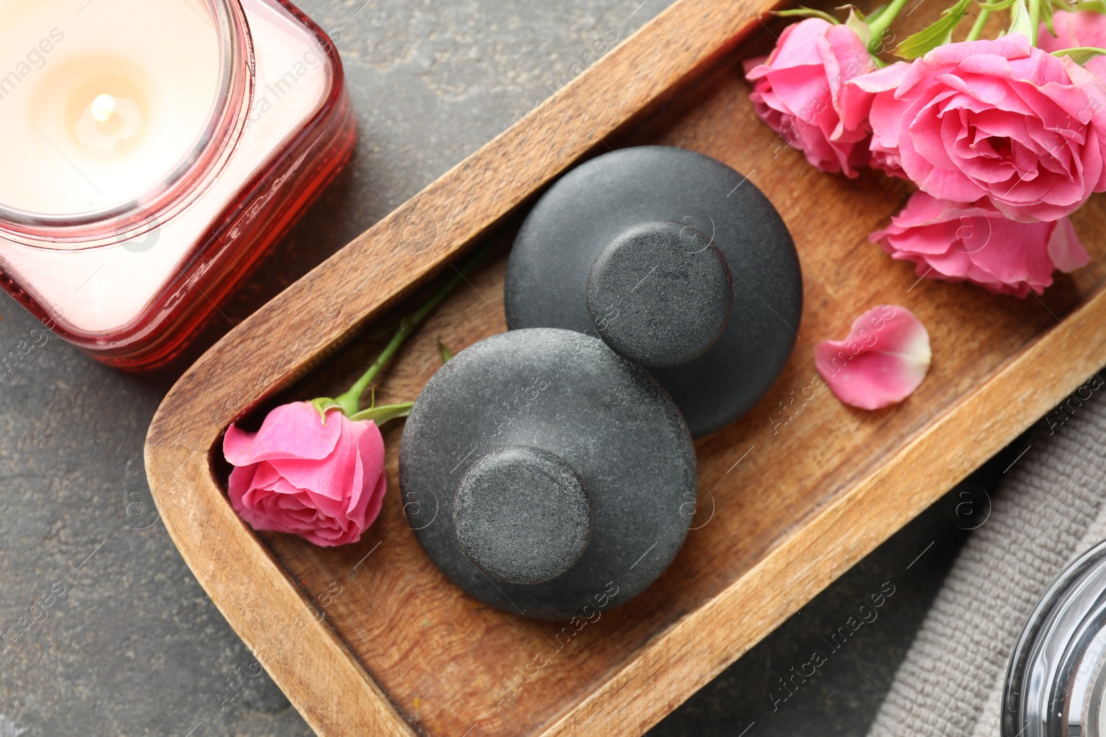 Photo of Spa stones, rose flowers and burning candle on grey table, top view