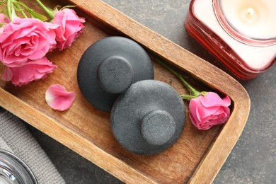 Photo of Spa stones, rose flowers and burning candle on grey table, top view