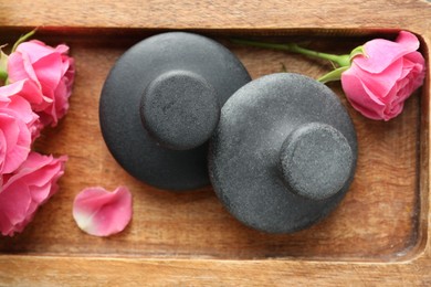 Photo of Spa stones and rose flowers on wooden tray, top view