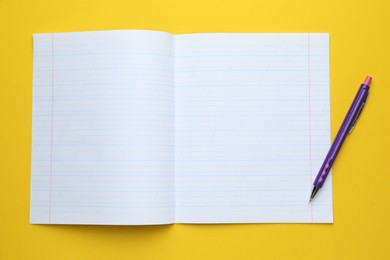 Photo of Open copybook and pen on yellow background, top view