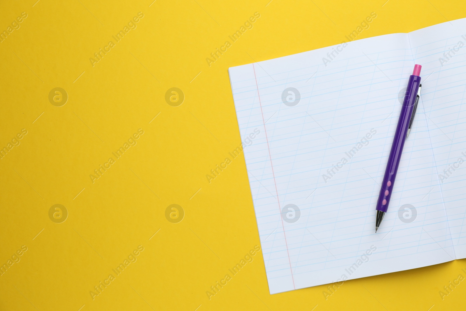 Photo of Open copybook and pen on yellow background, top view. Space for text