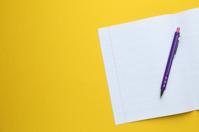 Photo of Open copybook and pen on yellow background, top view. Space for text