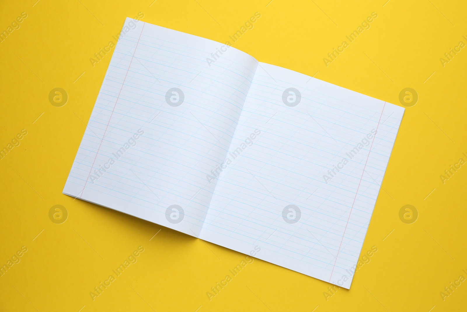 Photo of Open copybook on yellow background, top view