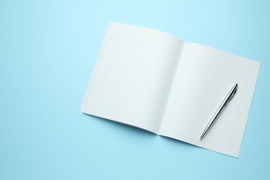 Photo of Open copybook and pen on light blue background, top view. Space for text