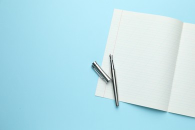 Photo of Open copybook and fountain pen on light blue background, top view. Space for text