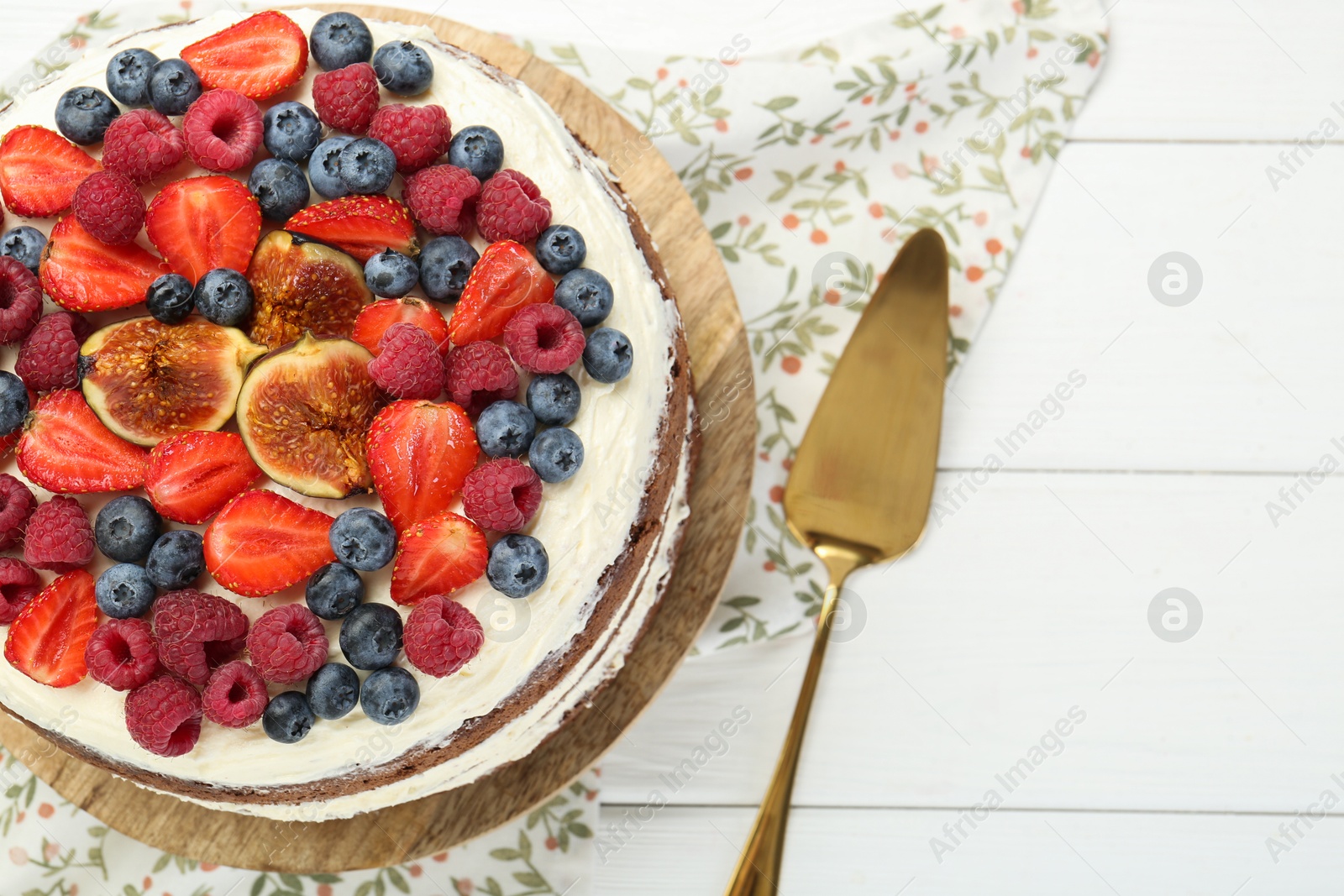 Photo of Delicious chocolate sponge cake with berries and server on white wooden table, top view