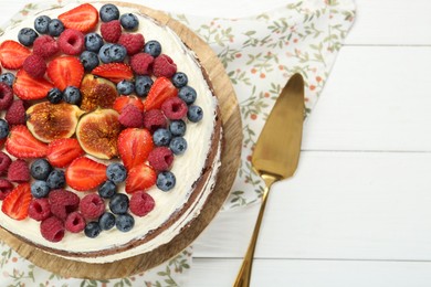 Photo of Delicious chocolate sponge cake with berries and server on white wooden table, top view