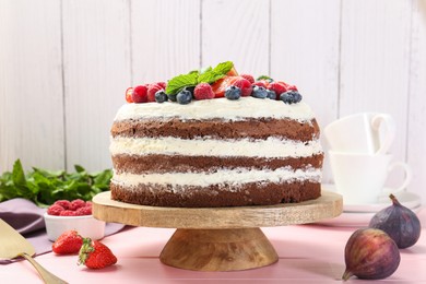 Photo of Delicious chocolate sponge cake with berries served on pink wooden table