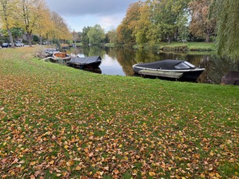 Photo of Beautiful view of canal with moored boats and colorful fallen leaves on autumn day