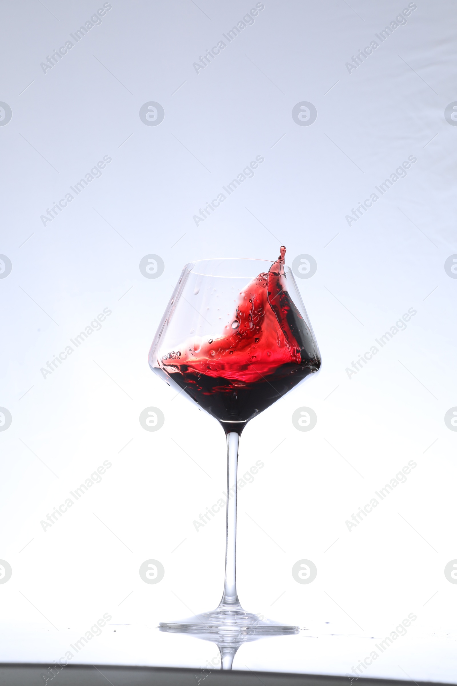 Photo of Red wine splashing in glass on white background