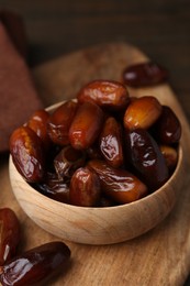 Photo of Tasty sweet dried dates in bowl on wooden board, closeup