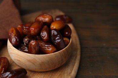 Photo of Tasty sweet dried dates in bowl on wooden table, closeup. Space for text