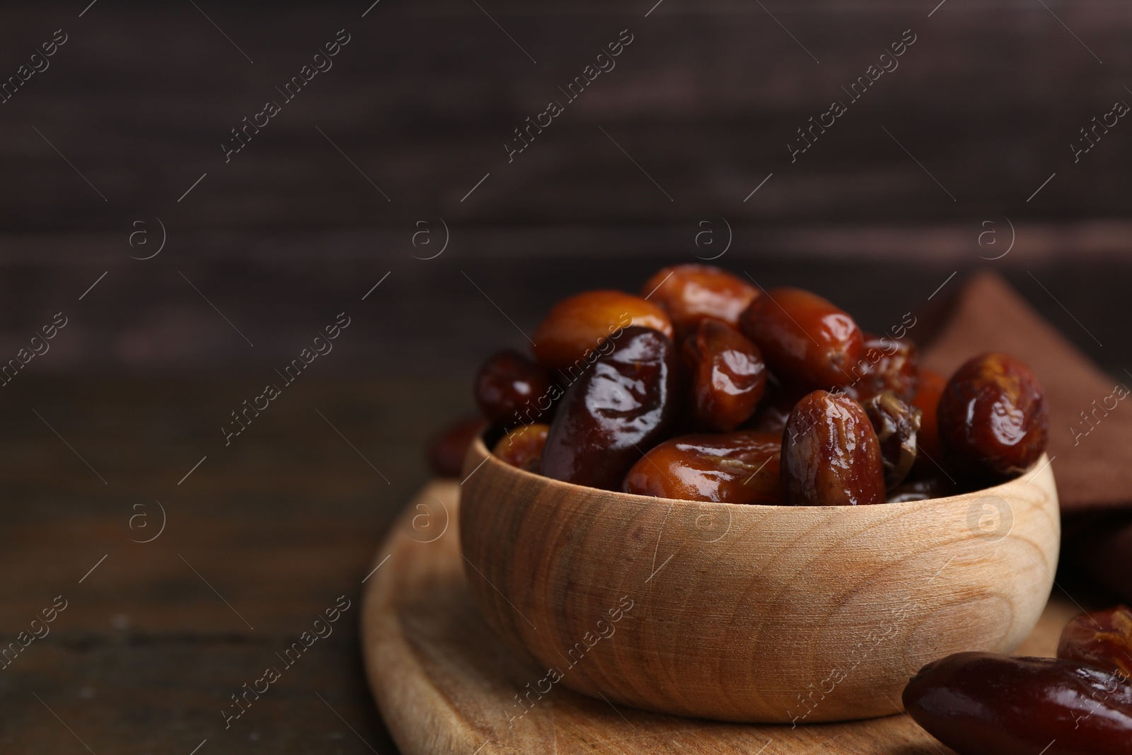 Photo of Tasty sweet dried dates in bowl on wooden table, closeup. Space for text