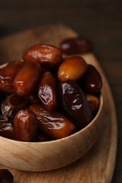 Photo of Tasty sweet dried dates in bowl on wooden board, closeup