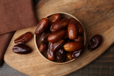 Photo of Tasty sweet dried dates in bowl on wooden table, top view