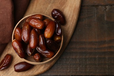 Photo of Tasty sweet dried dates in bowl on wooden table, top view. Space for text