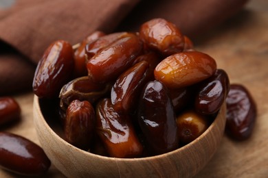 Photo of Tasty sweet dried dates in bowl on wooden table, closeup