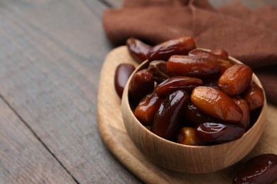 Photo of Tasty sweet dried dates in bowl on wooden table, closeup. Space for text