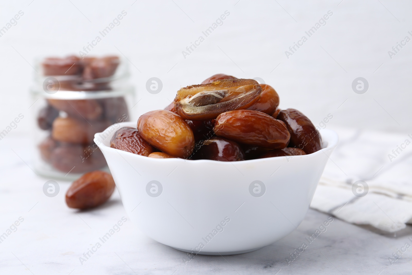 Photo of Tasty dried dates in bowl and jar on white marble table, closeup