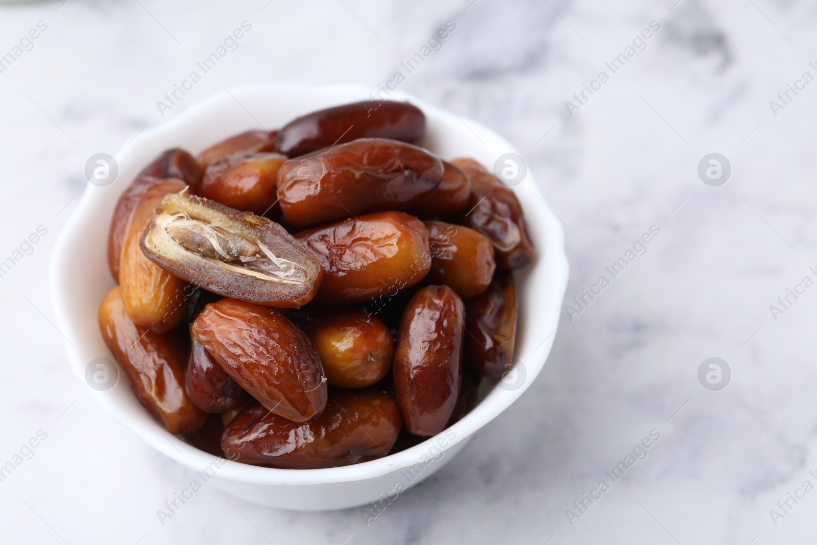 Photo of Tasty dried dates in bowl on white marble table, closeup. Space for text