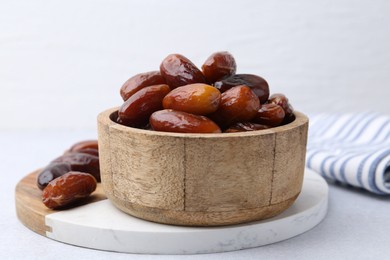 Photo of Tasty dried dates in wooden bowl on white table, closeup