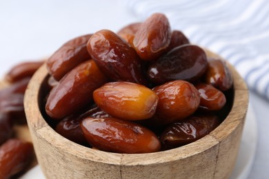 Photo of Tasty dried dates in wooden bowl on white table, closeup