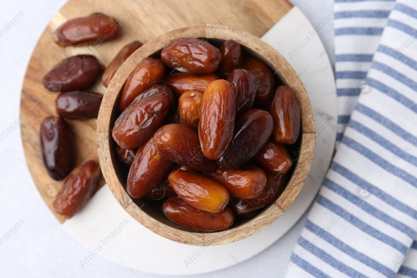 Photo of Tasty dried dates in wooden bowl on white table, top view