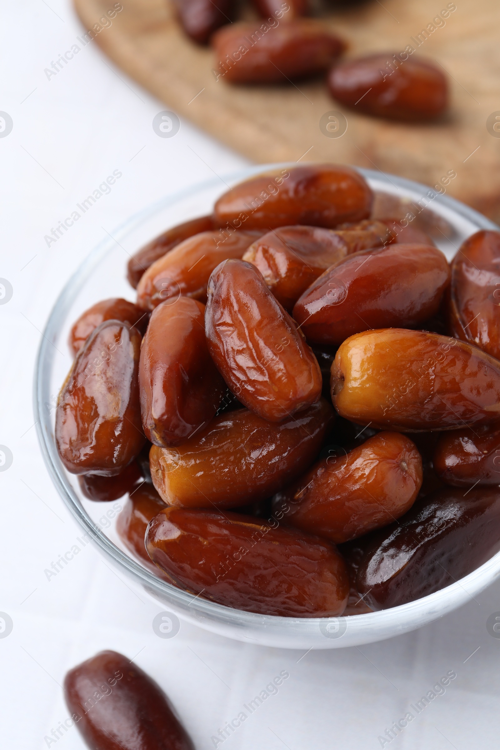 Photo of Tasty dried dates in glass bowl on white table, closeup