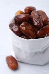 Photo of Tasty sweet dried dates in paper bag on white table, closeup