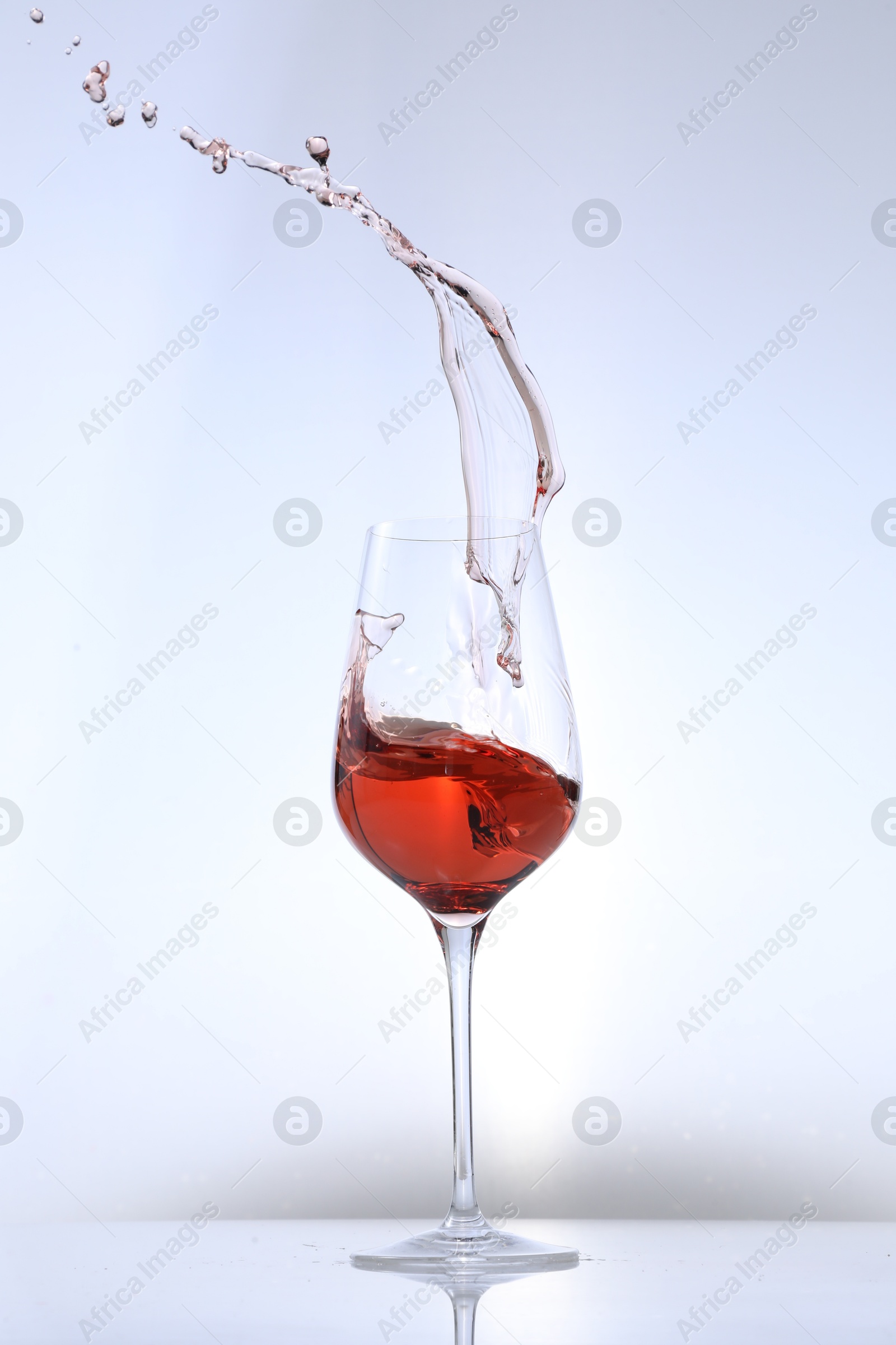 Photo of Rose wine splashing in glass on white background