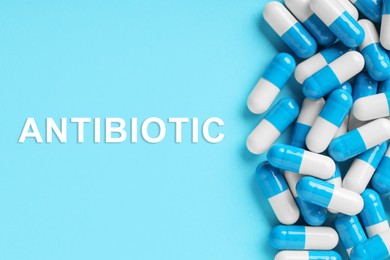 Word Antibiotic and pills on light blue background, top view